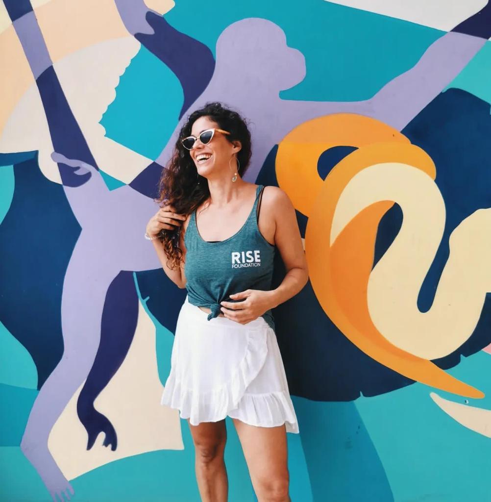 real estate agent claudia figueras standing in front of the colourful RISE Caribe mural